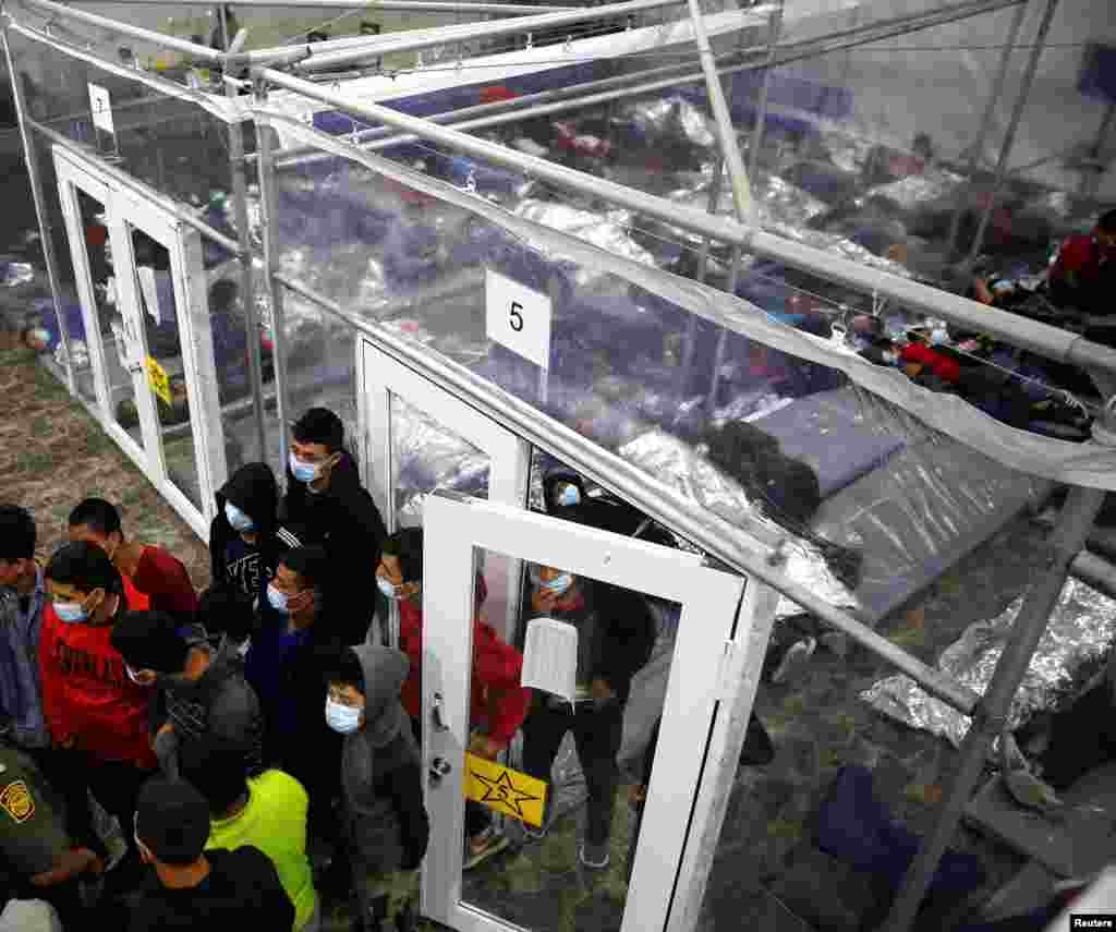 Jóvenes migrantes hablan con un agente fuera de una cápsula en el centro de detención.