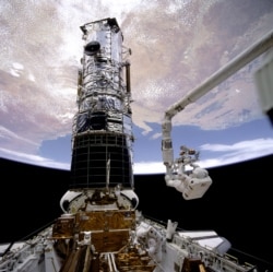 Astronaut F. Story Musgrave, anchored on the end of the Remote Manipulator System (RMS) arm, prepares to be elevated to the top of the Hubble Space Telescope (HST) to install protective covers on the magnetometers. Astronaut Jeffrey A. Hoffman inside payload bay, assisted Musgrave with final servicing tasks on the telescope, wrapping up five days of space walks. (Image Credit: NASA)