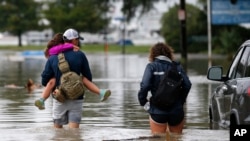 Don Noel carries his daughter Alexis, 8, with his wife Lauren, right as they walk through a flooded roadway to check on their boat in the West End section of New Orleans, Wednesday, June 21, 2017.
