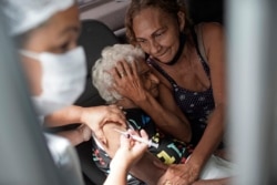 An elderly woman gets a shot of China's Sinovac CoronaVac vaccine as part of a priority COVID-19 vaccination program for the elderly at a drive-thru vaccination center in Rio de Janeiro, Brazil, Monday, Feb. 1, 2021.