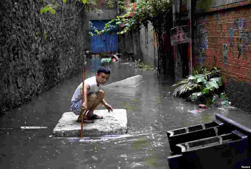2015年5月20日，广西柳州，强降雨让街上水流成河，有人蹲在发泡胶板上移动。
