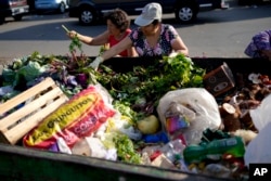Women collect vegetables to take home after they were discarded by vendors at a market on the outskirts of Buenos Aires, Argentina, Wednesday, Jan. 10, 2024. (AP Photo/Natacha Pisarenko)