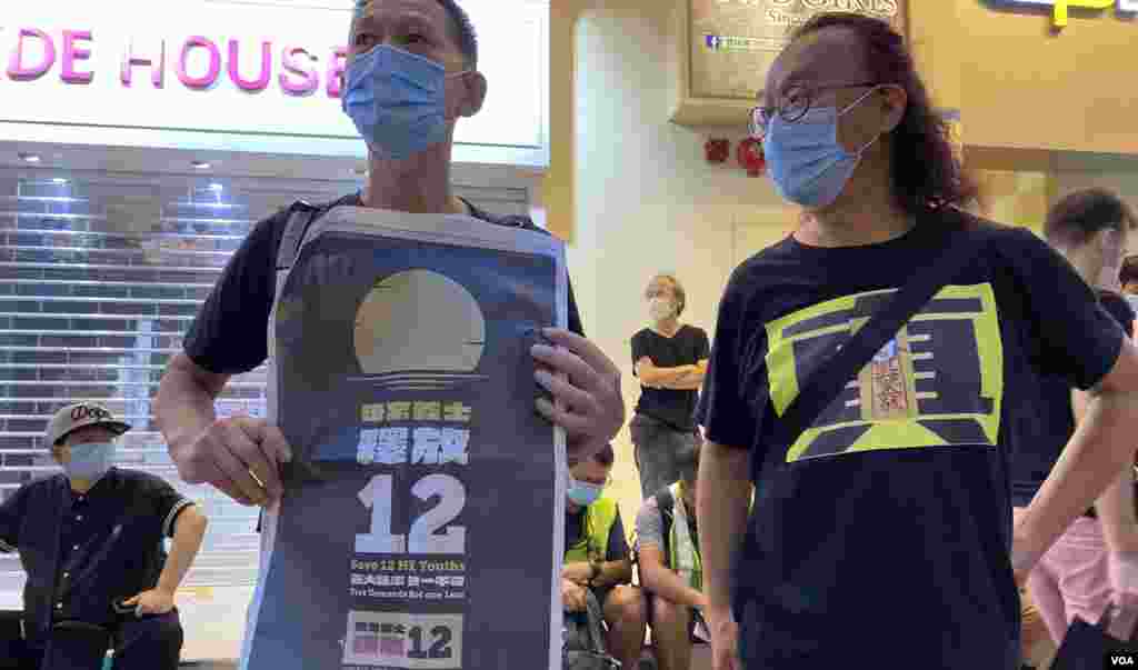 香港市民劉先生(左)10月1日在銅鑼灣行人專區手持印有釋放12港人標語的報章,批評中國當局利用12港人案製造恐慌及寒蟬效應,他又認為十一不是中國”國慶”而是”國殤”。(美國之音湯惠芸)
