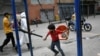 Un niño, con un tapabocas en la barbilla, juega junto a un trabajador de la ciudad que rocía desinfectante en una calle del barrio Catia, en Caracas, Venezuela.