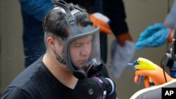 A Servpro cleaning worker has his respirator mask sprayed down Thursday, March 12, 2020, as he gets ready for a break from his work cleaning inside the Life Care Center in Kirkland, Wash., near Seattle. (AP Photo/Ted S. Warren)